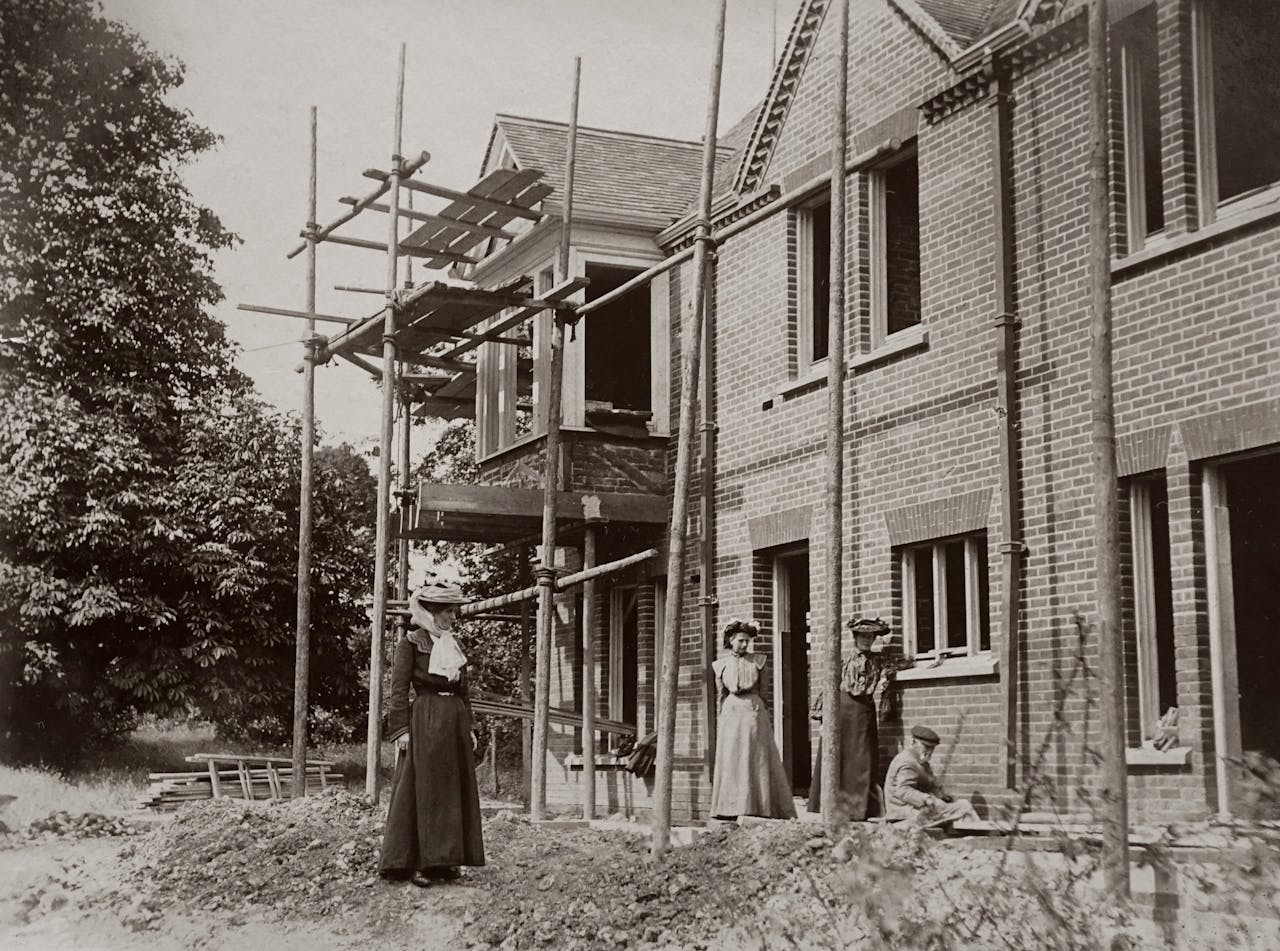 Vintage photo of an Edwardian house under construction with people observing.